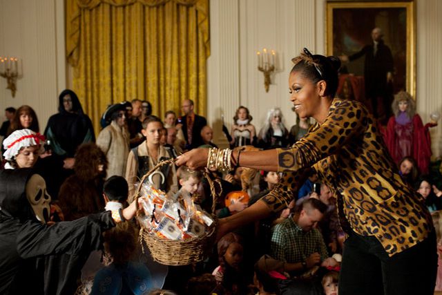 A purr-fectly costumed Michelle Obama distributes what can only be healthy, organically grown, locally-sourced fruit treats to children on Halloween.